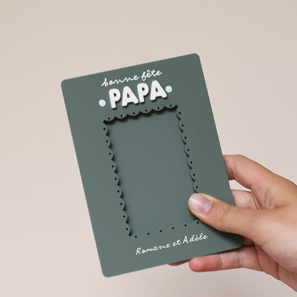 Cadre en plexi, format rectangulaire colors vert « pin » et texte blanc. Découpe de l’ouverture au centre en feston 
Inscription en haut centré sur 2 lignes, ligne 1 « bonne fête », ligne 2 « Papa » en relief plexi blanc et sur les côtés du mot 2 smileys imprimés
Inscription en bas de deux prénoms